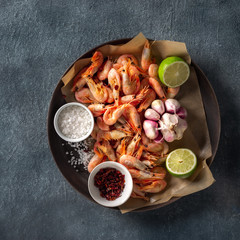 Raw shrimp in a pan with ingredients for cooking on a dark background top view