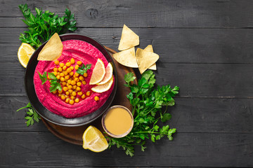 Tasty and healthy food concept. Fresh beetroot hummus in plate with chickpeas and pita bread on dark background top view