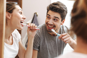 Image of joyful couple cleaning teeth together in bathroom