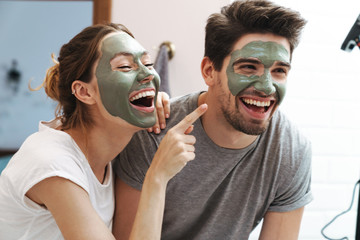 Image of caucasian couple standing in bathroom with face mask