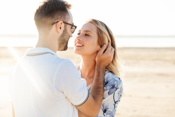 Photo of attractive romantic couple smiling and hugging while walking on sunny beach