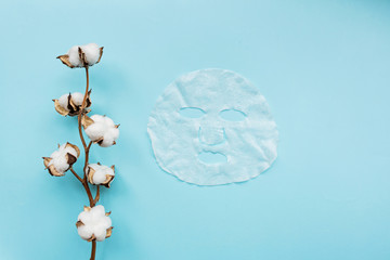 Sheet facial mask and cotton flower on pastel blue paper background. Skin care, dermatology, beauty concept. Top view, flat lay, mockup, overhead, copy space, template
