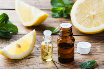 Essential lemon oil in bottle, fresh fruit slices on wooden background. Natural fragrances.