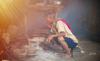 Old man with cream-colored shirts and plaid scarves in the countryside of asia is cooking, Country kitchen with sunshine, Simple living in the countryside concept.
