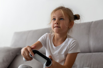 Enthusiastic kid in casual outfit playing with joystick while sitting on sofa in living-room