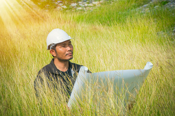 Engineer sitting in the field with blueprint Corporate Achievement Planning, Strategic planning, analysis of new architectural plans, Strategies and engineering risk concept.