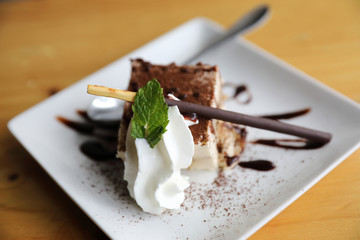 tiramisu cake dessert with cream mint and chocolate sauce on wood background