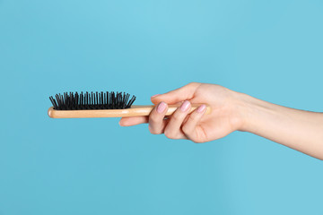 Naklejka premium Woman holding wooden hair brush against blue background, closeup
