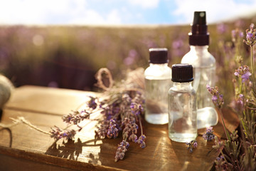 Obraz na płótnie Canvas Bottles of lavender essential oil on wooden table in field