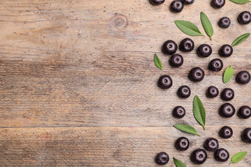 Fresh acai berries with leaves on wooden table, flat lay. Space for text