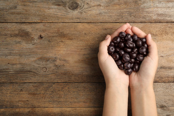 Top view of woman holding fresh acai berries on wooden background, closeup. Space for text