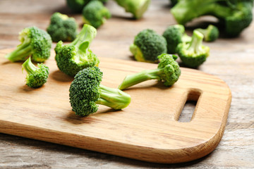 Wooden board with fresh broccoli florets on table, closeup