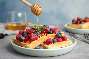 Pouring honey onto delicious waffles with fresh berries served on grey table