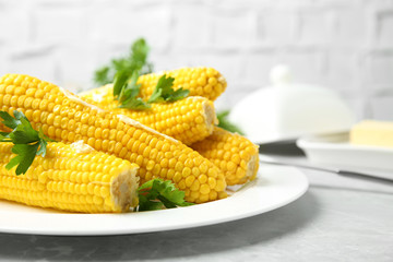 Plate of boiled corn cobs with butter and parsley on light grey table, closeup. Space for text