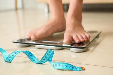 Tape in front of woman standing on floor scales indoors. Overweight problem - obrazy, fototapety, plakaty