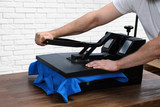 Man using heat press machine at table near white brick wall, closeup