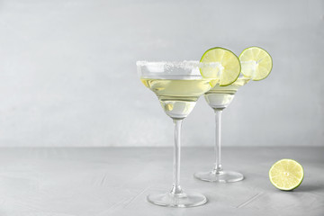 Glasses of lemon drop martini cocktail with lime slice on light table against grey background. Space for text