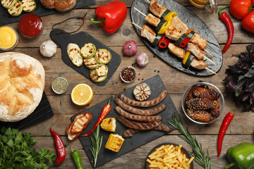 Flat lay composition with barbecued meat and vegetables on wooden table