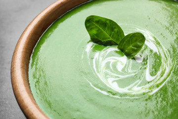 Bowl of healthy green soup with fresh spinach on grey table, closeup view