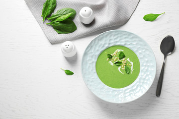 Plate of healthy green soup with fresh spinach served on white wooden table, flat lay. Space for text