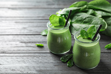 Jars of healthy green smoothie with fresh spinach on grey wooden table. Space for text