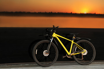 Obraz premium Yellow bicycle parked near glass building at sunset