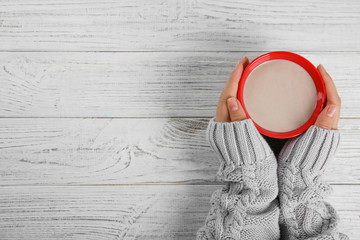 Woman holding cup of hot cocoa at white wooden table, top view with space for text. Winter drink