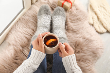 Woman with cup of hot mulled wine sitting on window sill, above view. Winter drink