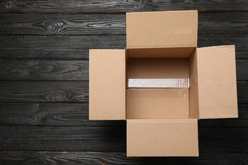 Open cardboard box on black wooden background, top view. Space for text