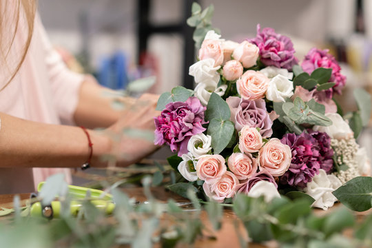 Close-up flowers in hand. Florist workplace. Woman arranging a bouquet with roses, carnation and other flowers. A teacher of floristry in master classes or courses