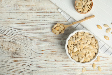 Flat lay composition with raw pumpkin seeds on white wooden table, space for text