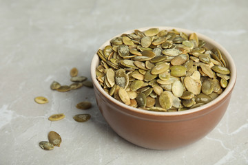 Bowl of raw pumpkin seeds on light grey marble table. Space for text