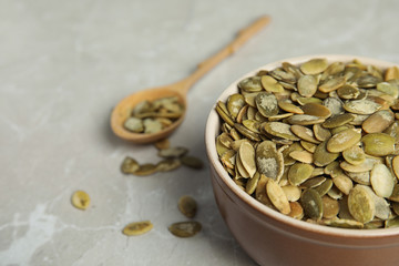 Bowl of raw pumpkin seeds on light grey marble table, closeup. Space for text