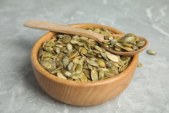 Bowl and spoon of raw pumpkin seeds on light grey marble table
