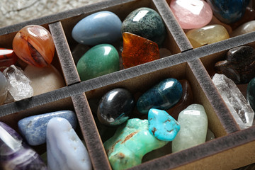 Box with different beautiful gemstones on table, closeup