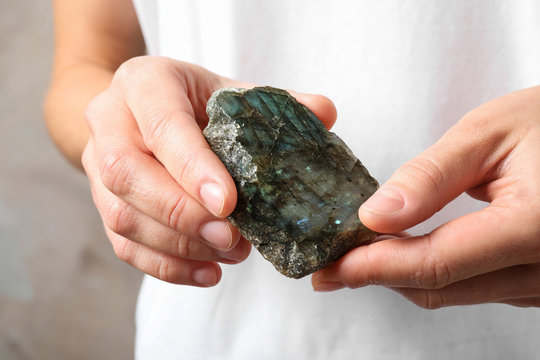 Young woman holding beautiful labradorite gemstone on beige background, closeup