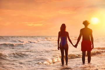 Young woman in bikini and her boyfriend on beach at sunset. Lovely couple