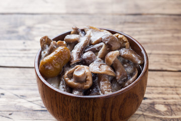 Stewed mushrooms in a sauce with sour cream and cheese in a wooden bowl.