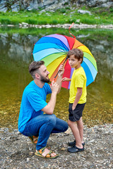Fathers day outdoor. Father and son under a rainbow color umbrella