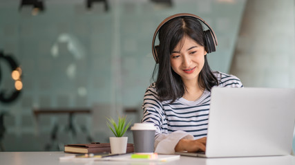 Young women using laptop and listening song in on-ear headphones.