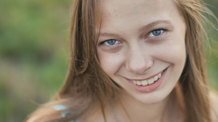 Portrait of a young smiling sixteen-year-old girl with a daisy flower in her hands. Brown-haired girl with long hair.. Face close-up.