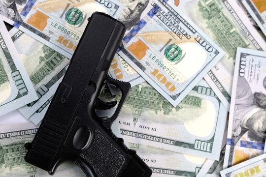 profit from criminal activity. .proceeds of crime. black metal pistol, gun on a pile of american 100 dollar bills