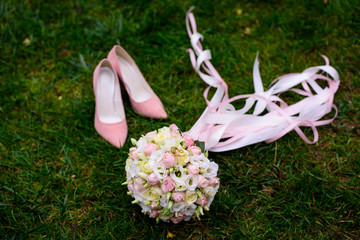 Bride's shoes with bouquet and rings on green textural grass