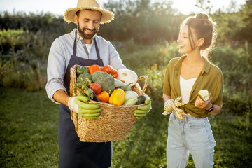 Portrait of a man and woman holding basket full of freshly picked up homegrown vegetables at the...