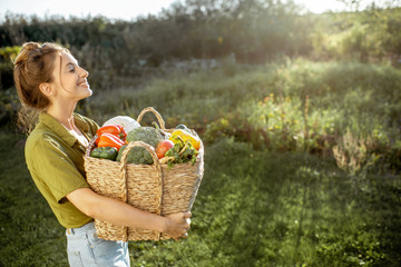 Portrait of a beautiful young woman with basket full of freshly picked up vegetables standing in...