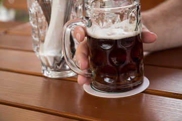 Mann trinkt Glas dunkles Landbier oder Vollbier Bier in Biergarten auf Holz Tisch im Sommer