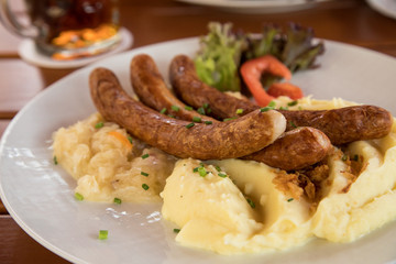 Bayrische Bayreuther Bratwürste mit Sauerkraut und Kartoffelpüree auf Holz Tisch Hintergrund in Biergarten
