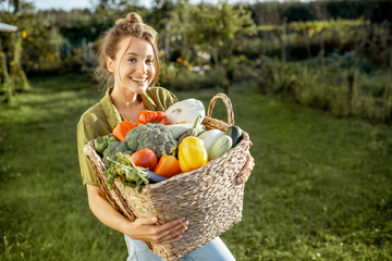 Portrait of a beautiful young woman with basket full of freshly picked up vegetables standing in...