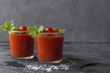 Halloween Bloody Mary cocktails served with pickled veggies (tomatos, olive and celery) and paper bats on a dark background.