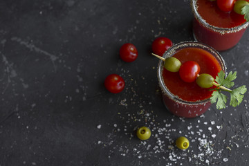 Spicy Vodka Bloody Mary cocktails served with pickled veggies (tomatos, olive and celery) on a dark background.